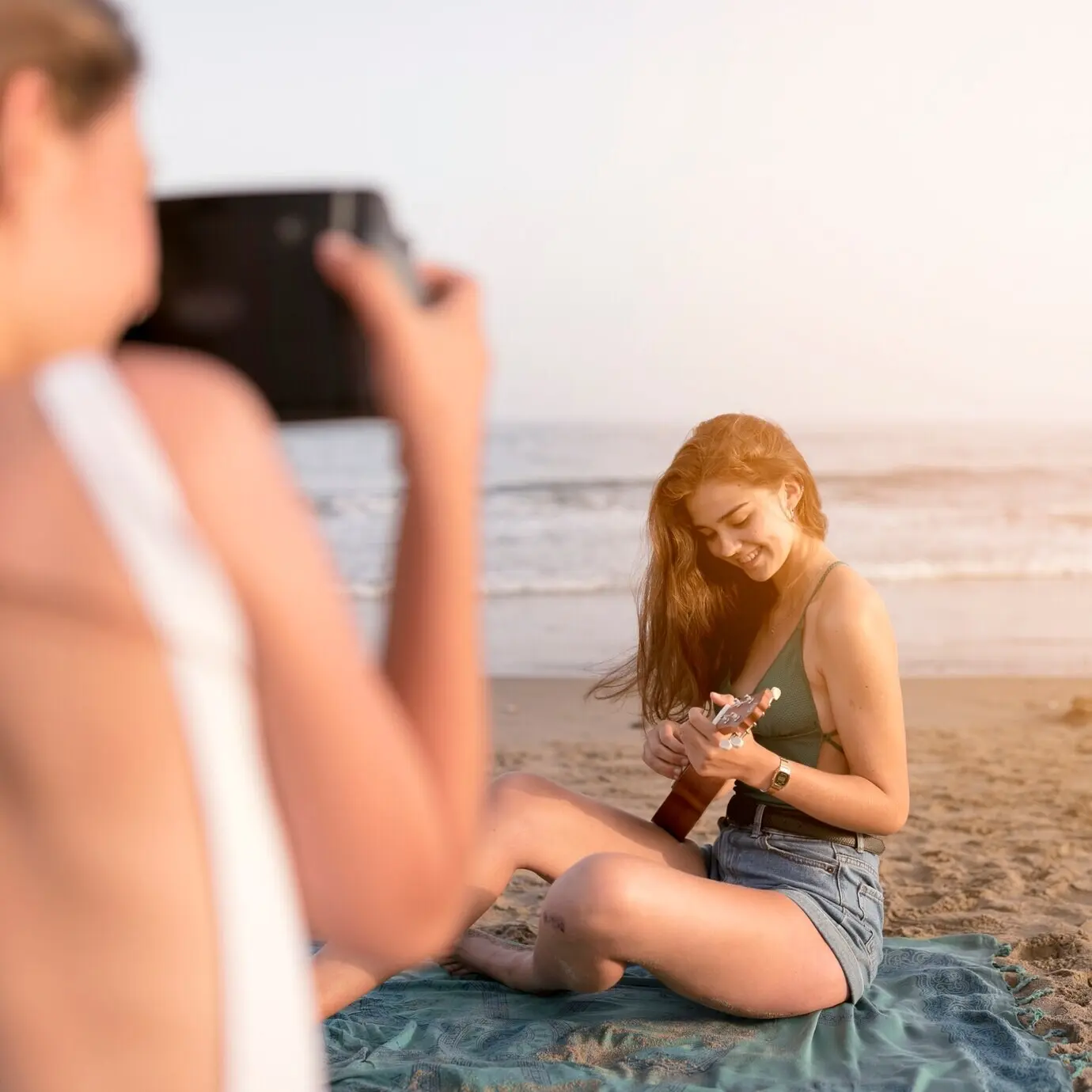 Ein Freund macht ein Selfie von einem Mädchen, das am Strand Ukulele spielt.